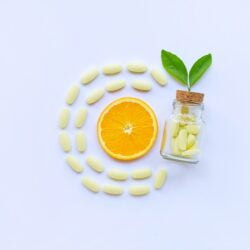 Vitamin C bottle and pills with orange fruit on white.