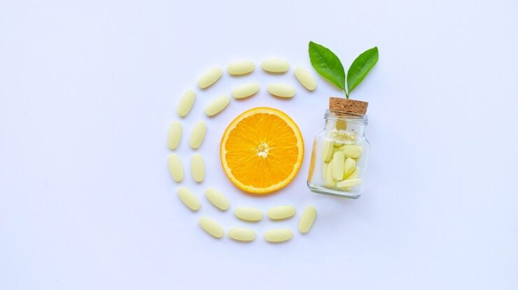 Vitamin C bottle and pills with orange fruit on white.